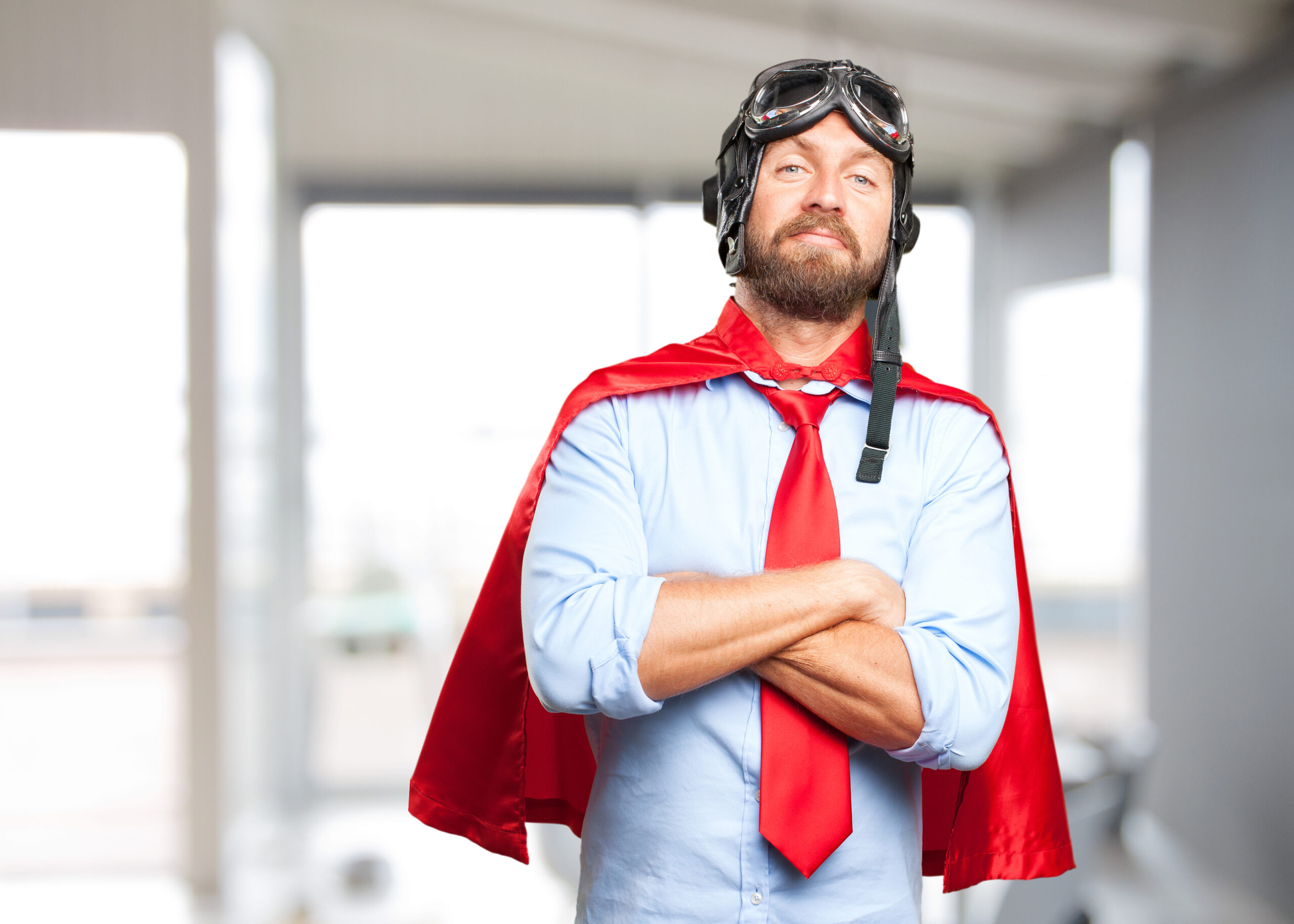 Homem de capa vermelha, óculos de aviador e braços cruzados, posando como super-herói